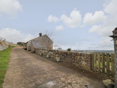 A stone house with a sloped driveway and stone wall with potted plants on the side at Healey Farm Cottage in Rothbury