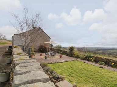 An outdoor patio with a table and umbrella next to a stone building and a grass lawn at Healey Farm Cottage in Rothbury