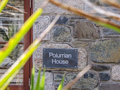 A stone wall with a sign that says Polurrian House next to a wooden door partially obscured by green plants at Polurrian House in Cury near Mullion