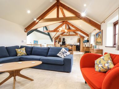 A living area with a blue sectional sofa, an orange armchair, and a wooden coffee table under wooden ceiling beams at Polurrian House in Cury near Mullion