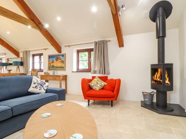A living room with a blue sofa a red armchair a wooden coffee table a black wood stove and wooden beams at Polurrian House Cury near Mullion