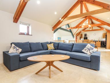 A living room with a blue sectional sofa and wooden coffee table under exposed wooden beams at Polurrian House in Cury near Mullion