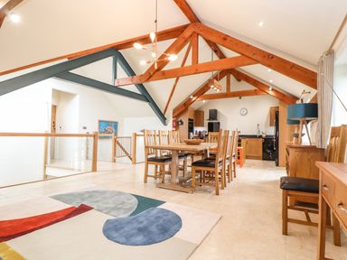 A dining area with wooden table and chairs near a kitchen with wooden cabinets and visible ceiling beams at Polurrian House in Cury near Mullion