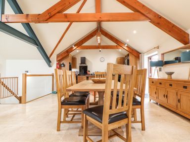 A dining area with wooden table and chairs under exposed wooden beams at Polurrian House in Cury near Mullion