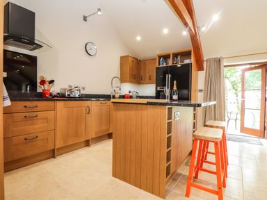 A kitchen with wooden cabinets a black refrigerator an island with two orange stools and an open door at Polurrian House in Cury near Mullion