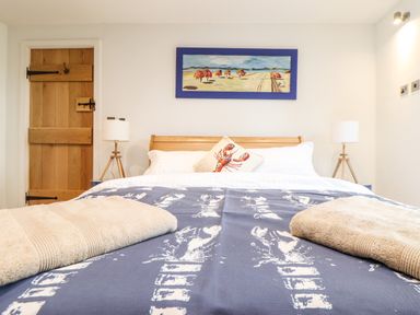 A bedroom with a wooden bed and bedside lamps with a door and a painting at Polurrian House in Cury near Mullion