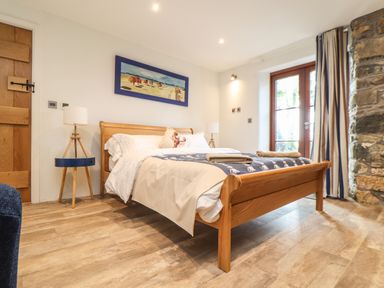 A bedroom with a wooden bed and bedside tables with lamps at Polurrian House in Cury near Mullion