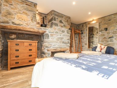 A bedroom with a wooden dresser blue bedding a chair with a lobster pillow and a large mirror at Polurrian House in Cury near Mullion