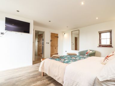 A bedroom with a bed a wall-mounted television wooden doors a chair and a mirror at Polurrian House Cury near Mullion