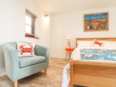 A bedroom with a wooden bed and a light blue armchair with crab cushions at Polurrian House in Cury near Mullion