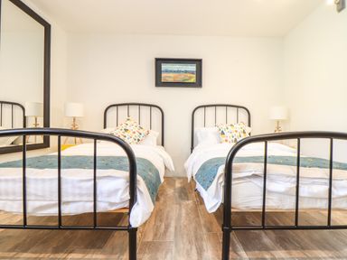 A bedroom with two single beds with black frames white bedding and blue throws with patterned pillows a large mirror a wooden floor two bedside lamps and a framed picture on the wall at Polurrian House in Cury near Mullion