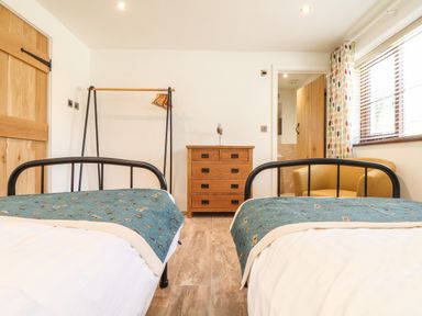 A bedroom with two single beds a wooden chest of drawers and an armchair at Polurrian House in Cury near Mullion