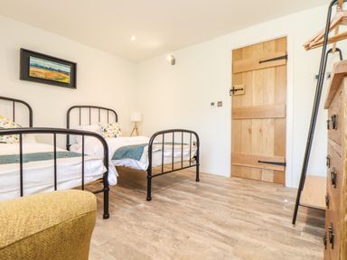 A bedroom with two single metal frame beds a wooden door a wooden dresser and a lamp at Polurrian House in Cury near Mullion