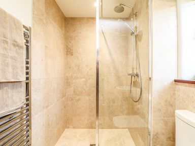 A bathroom with a glass-enclosed shower, tiled walls and floor, a shower head, a towel rack with towels, and a toilet at Polurrian House in Cury near Mullion