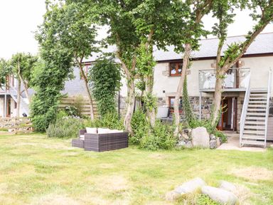 A garden with trees and outdoor seating in front of a stone house with a metal staircase at Polurrian House in Cury near Mullion