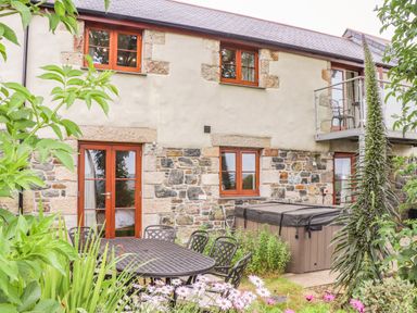 An outdoor patio area with a metal table and chairs hot tub and plants in front of a stone house at Polurrian House in Cury near Mullion
