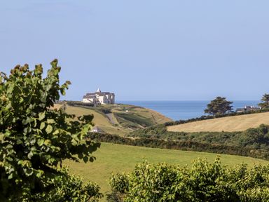 A landscape with a large house on a hill overlooking the sea and fields with trees in Cury near Mullion