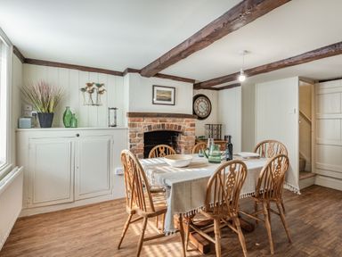 A dining room with a wooden table and chairs a brick fireplace and wooden ceiling beams at Smugglers Cottage in Christchurch