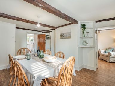A dining room with wooden chairs and table set with plates glasses and a bottle at Smugglers Cottage in Christchurch