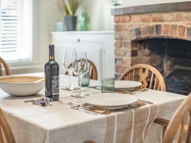 A dining table set with plates glasses a wine bottle and cutlery near a brick fireplace at Smugglers Cottage in Christchurch