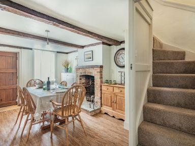 A dining room with a wooden table and chairs near a brick fireplace and carpeted stairs at Smugglers Cottage in Christchurch