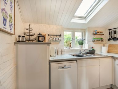 A kitchen with a dishwasher a sink a kettle hanging mugs and spice racks at Smugglers Cottage in Christchurch