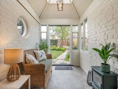 A sunroom with wicker sofa cushions table lamp and a green stove at Smugglers Cottage in Christchurch