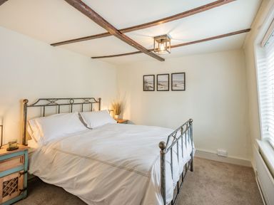 A bedroom with a metal bed frame two bedside tables lamps and three framed pictures on the wall at Smugglers Cottage in Christchurch