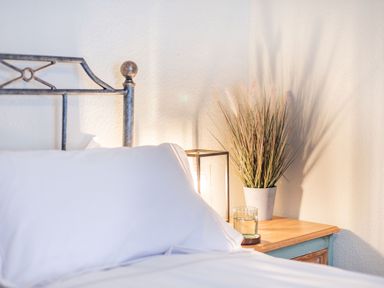 A bedside table with a glass of water a potted plant and a lamp next to a bed with white pillows at Smugglers Cottage in Christchurch