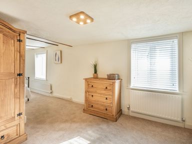 A bedroom area with a wooden chest of drawers a wardrobe and windows with blinds at Smugglers Cottage in Christchurch