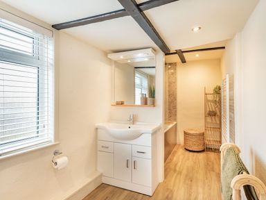 A bathroom with a sink cabinet mirror window wooden floor and towel rack at Smugglers Cottage in Christchurch