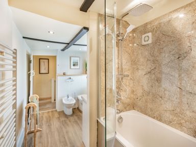 A bathroom with a bathtub and shower unit bidet and toilet with wooden floor at Smugglers Cottage Christchurch
