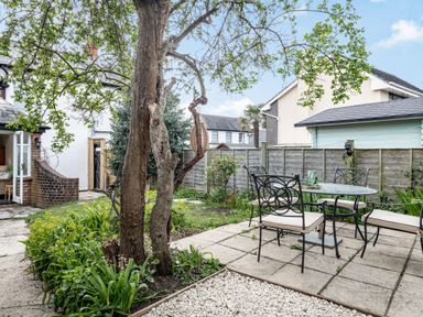 A backyard with a large tree a patio table and four chairs surrounded by plants and a fence at Smugglers Cottage in Christchurch