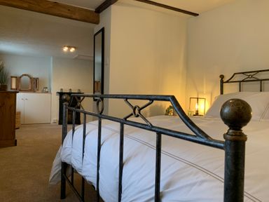 A bedroom with a metal bed frame white bedding a wooden dresser a cabinet and a mirror at Smugglers Cottage in Christchurch