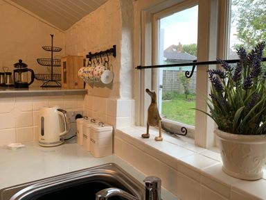 A kitchen corner with a kettle canisters hanging mugs a wooden duck and a potted plant by a window at Smugglers Cottage in Christchurch