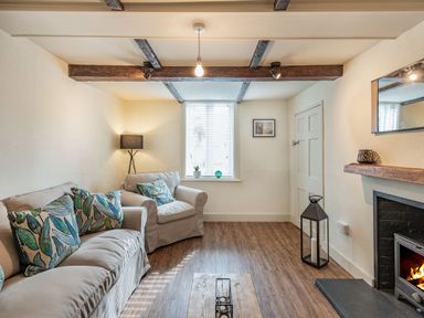 A living room with sofa armchair patterned cushions wood floor and fireplace at Smugglers Cottage in Christchurch