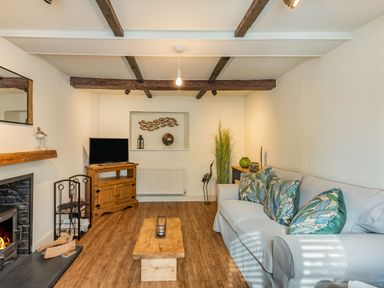 A living room with a fireplace a wooden coffee table a sofa with patterned cushions and a TV on a wooden stand at Smugglers Cottage Christchurch