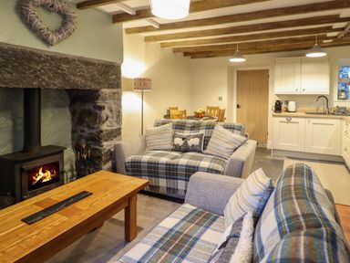 A living room with sofas covered in plaid blankets a wooden coffee table and a fireplace next to a kitchen and dining area at Bwthyn Y Bugail in Manod near Blaenau Ffestiniog