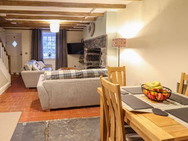 A living room with sofas a television a stone fireplace and a dining table with fruit bowl at Bwthyn Y Bugail in Manod near Blaenau Ffestiniog
