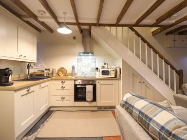 A kitchen with appliances under wooden beams next to a stairway with storage at Bwthyn Y Bugail Manod near Blaenau Ffestiniog