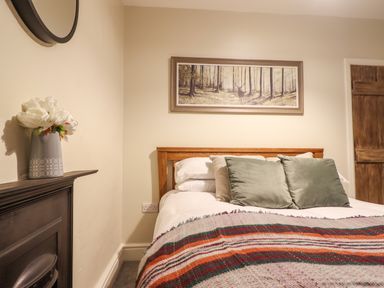 A bedroom with a wooden bed a striped blanket pillows a painting of a forest above the bed a flower vase on a mantel and a wooden door at Bwthyn Y Bugail in Manod near Blaenau Ffestiniog