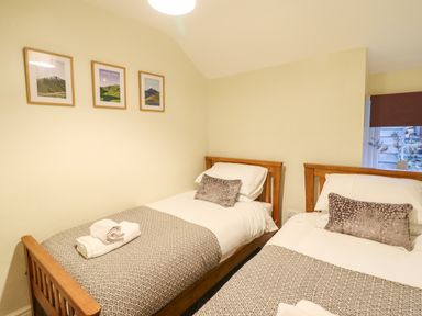 A bedroom with two single wooden beds with patterned throws and cushions and framed pictures on the wall at Bwthyn Y Bugail in Manod near Blaenau Ffestiniog