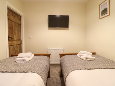A bedroom with two single beds with towels on them a wall-mounted TV a wooden door and a framed picture at Bwthyn Y Bugail Manod near Blaenau Ffestiniog
