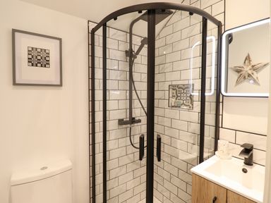 A bathroom with a shower enclosure with black frame a toilet a wooden vanity with a sink and a mirror with light at Bwthyn Y Bugail in Manod near Blaenau Ffestiniog