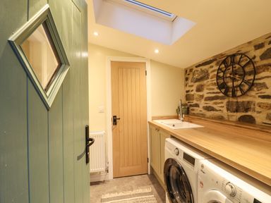 A laundry room with washing machines a wooden countertop a sink a stone wall clock and a wooden door at Bwthyn Y Bugail Manod near Blaenau Ffestiniog