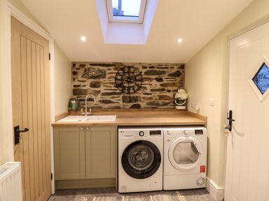 A laundry room with a washing machine and dryer under a wooden countertop and a sink with a faucet at Bwthyn Y Bugail Manod near Blaenau Ffestiniog
