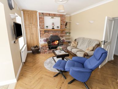 A living room with a blue recliner chair a sofa a brick fireplace and a wall-mounted television at The Water's Edge in Boyle County Roscommon