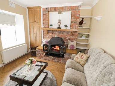 A living room with a brick fireplace a wood-burning stove a beige sofa and a coffee table with flowers at The Waters Edge in Boyle County Roscommon