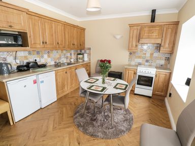 A kitchen with wooden cabinets a round dining table with four chairs and a vase of flowers at The Water's Edge in Boyle County Roscommon