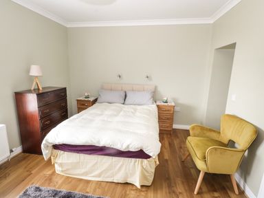 A bedroom with a bed a wooden chest of drawers two bedside tables and a yellow armchair at The Water's Edge in Boyle County Roscommon